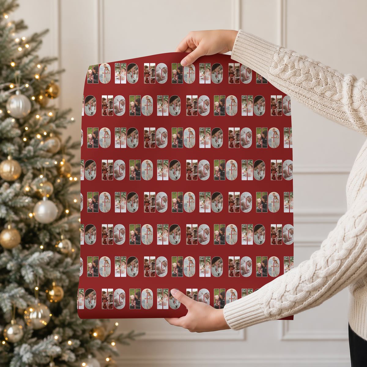 A person in a cream cable knit sweater holds up a large sheet of wrapping paper featuring a repeating Christmas themed pattern. The pattern consists of a red background with photos within the text 'HO HO HO'.