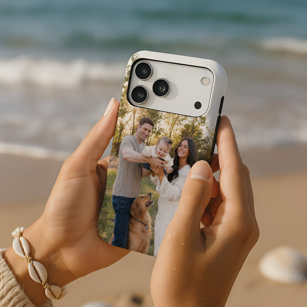 A person holds a smartphone with a custom printed photo case featuring a family and a dog, set against a blurred beach background.