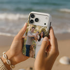 A person holds a smartphone with a custom printed photo case featuring a family and a dog, set against a blurred beach background.