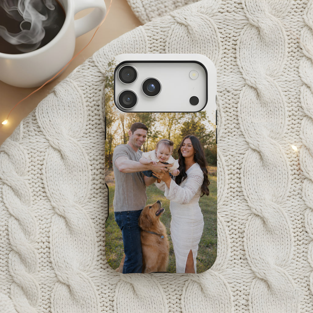 A custom photo printed on a smartphone case, displayed on a cream cable knit blanket next to a white coffee mug with steam.