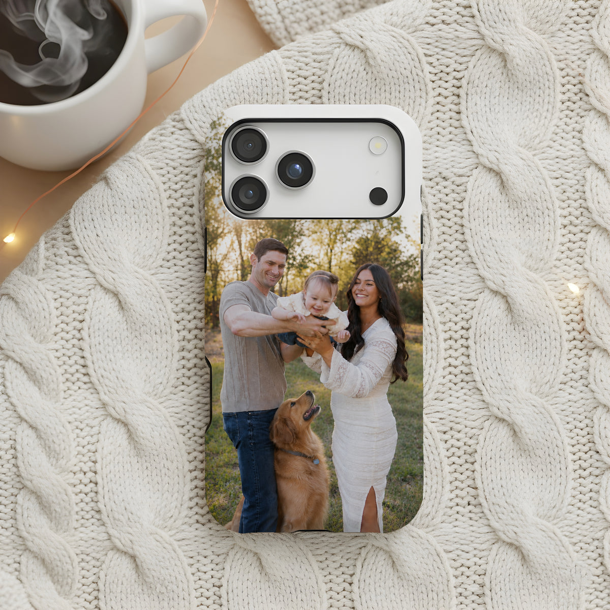 A custom photo printed on a smartphone case, displayed on a cream cable knit blanket next to a white coffee mug with steam.