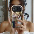 A person holds a smartphone in front of their face, showing a custom printed photo case on the phone. The case features a custom family photograph of a man, woman, and child with a golden retriever dog, displayed against a blurred indoor background.