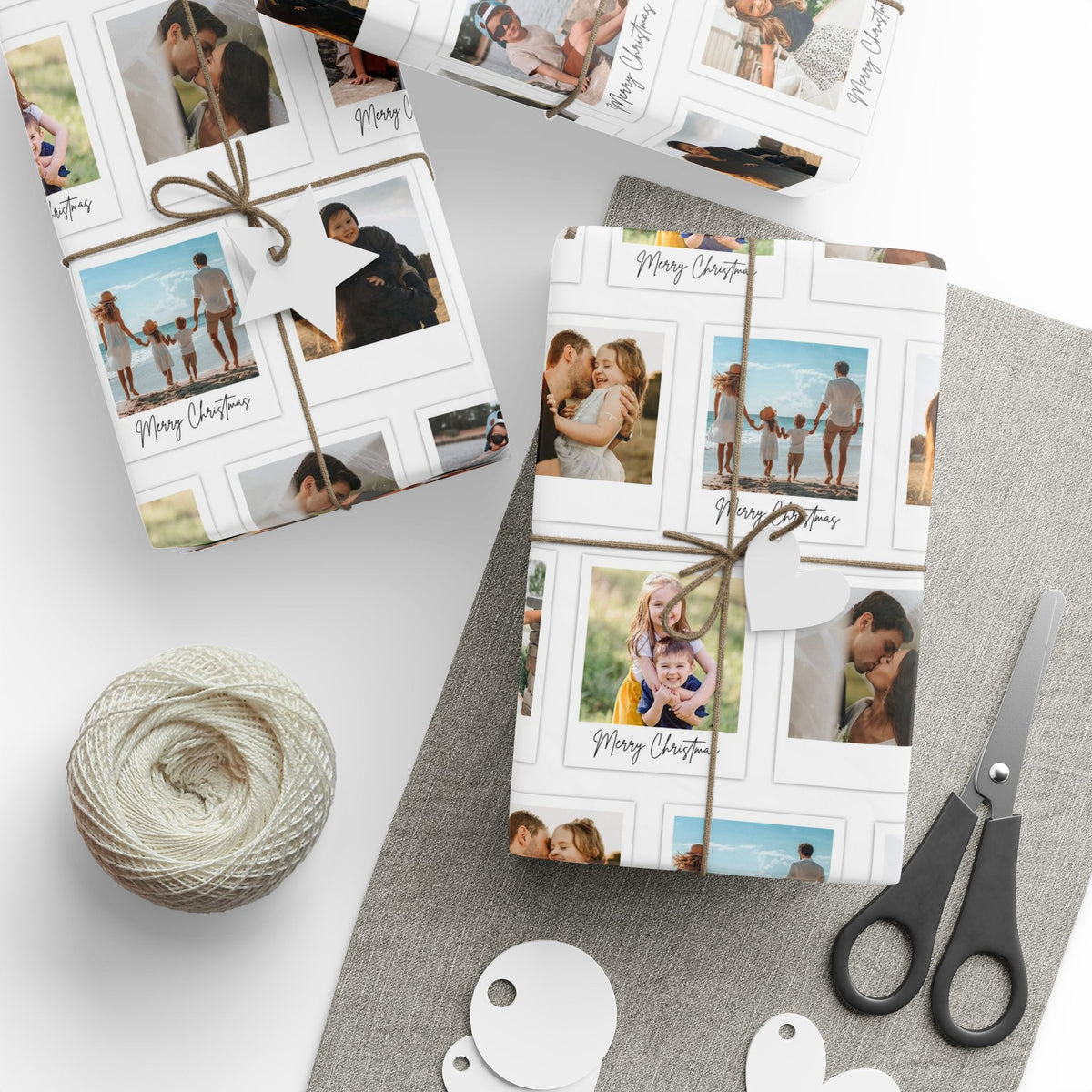 Three gift boxes wrapped in custom photo collage wrapping paper, tied with twine and a white star tag, arranged on a grey fabric surface with scissors, a ball of twine, and white round tags.