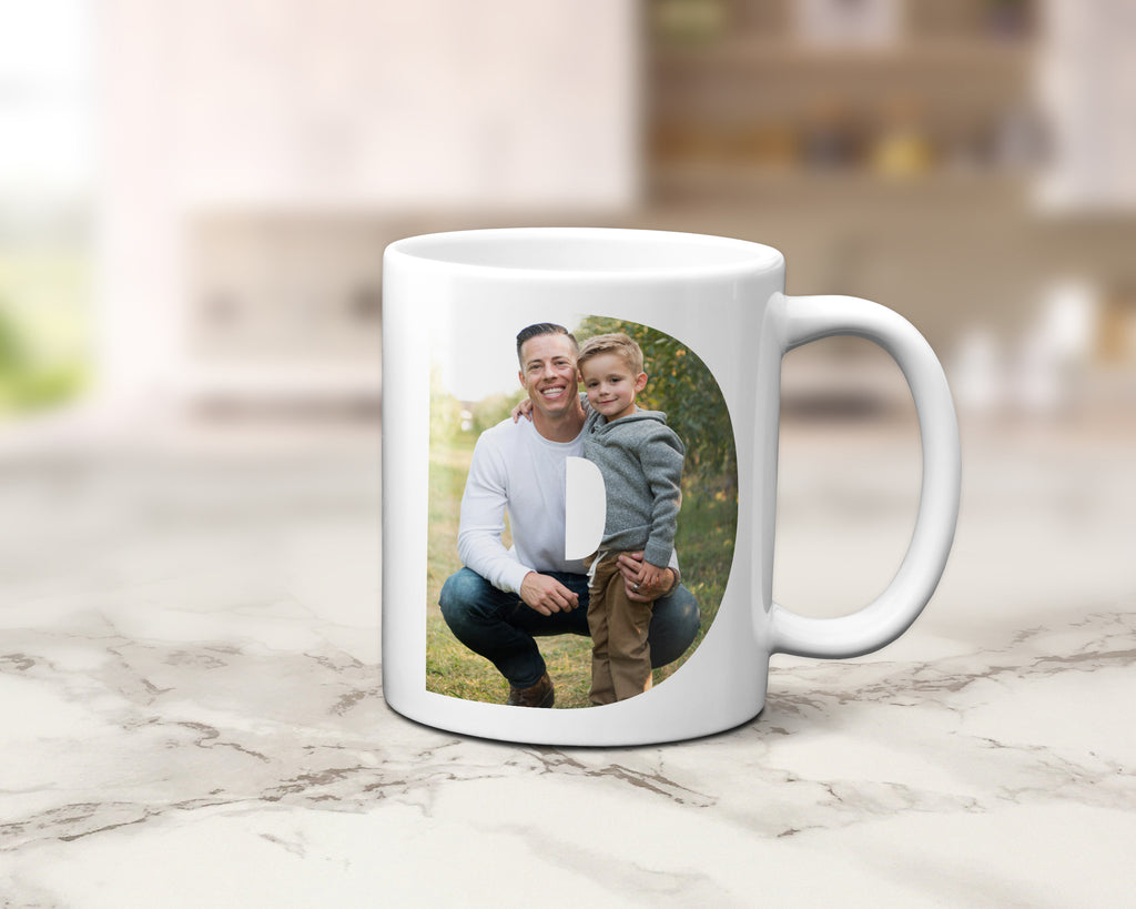 A white ceramic mug with a custom printed photo of a man and child, displayed on a light marble countertop with a blurred kitchen background.