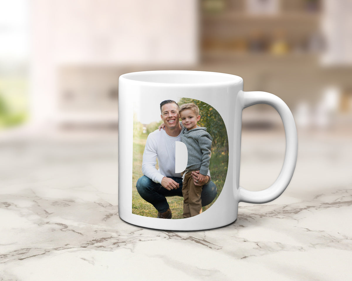 A white ceramic mug with a custom printed photo of a man and child, displayed on a light marble countertop with a blurred kitchen background.