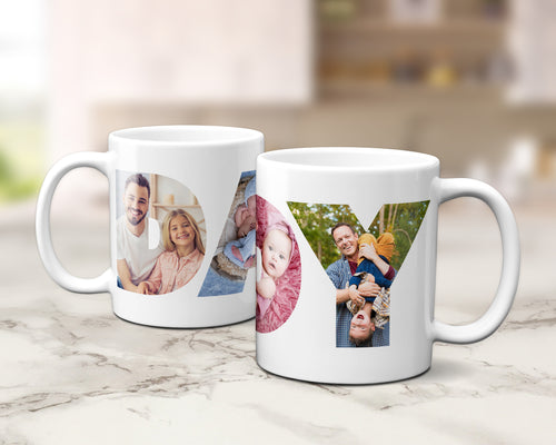 Two white ceramic mugs with custom family photos arranged inside large letters spelling 'DADDY', set on a light marble surface with a blurred kitchen background.