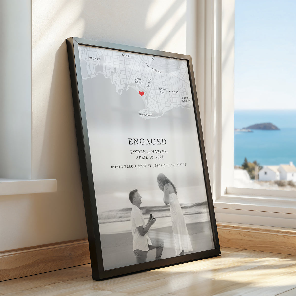 Framed custom engagement map print featuring a black and white map, red heart, ‘ENGAGED’ text, couple’s names and engagement date, with a couple portrait at the bottom
