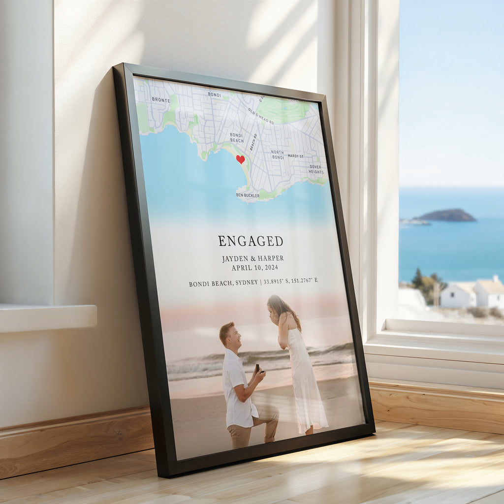 Framed custom engagement map print featuring a coloured map, red heart, ‘ENGAGED’ text, couple’s names and engagement date, with a couple portrait at the bottom