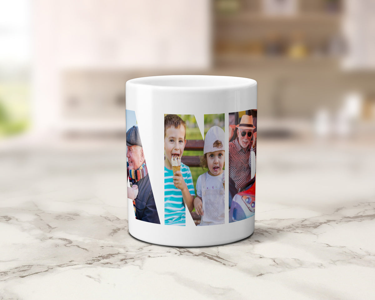 A white ceramic mug with a custom photo collage within the letters spelling 'GRANDAD', set on a light marble countertop with a blurred kitchen background.