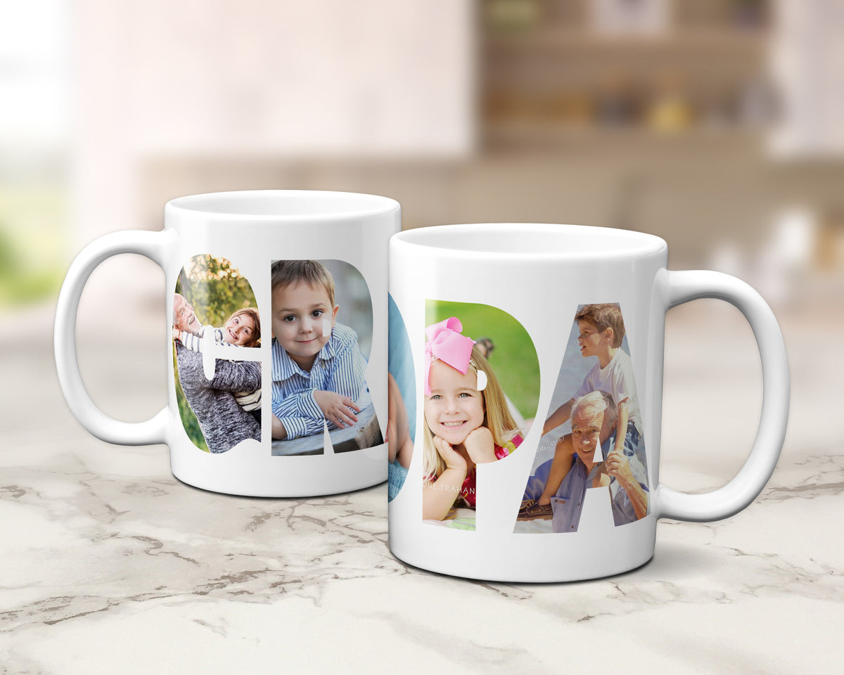 Two white ceramic mugs with custom photo filled letters spelling 'GRANDPA', displayed on a light marble surface with a blurred kitchen background.