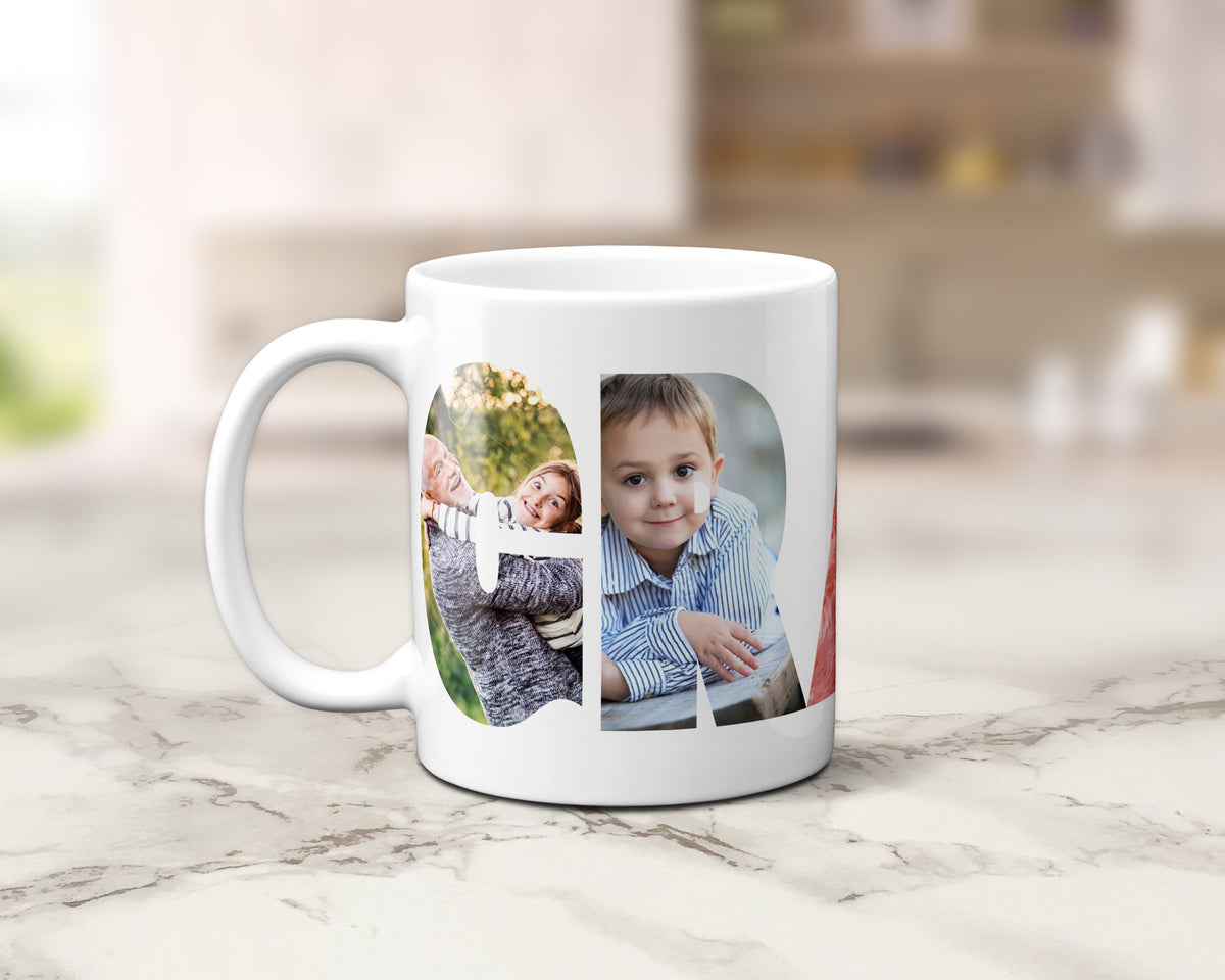 A white ceramic coffee mug with custom printed photos of a grandfather, a young girl and a young boy within the letters spelling GRANDPA, set on a light marble countertop with a blurred kitchen background.