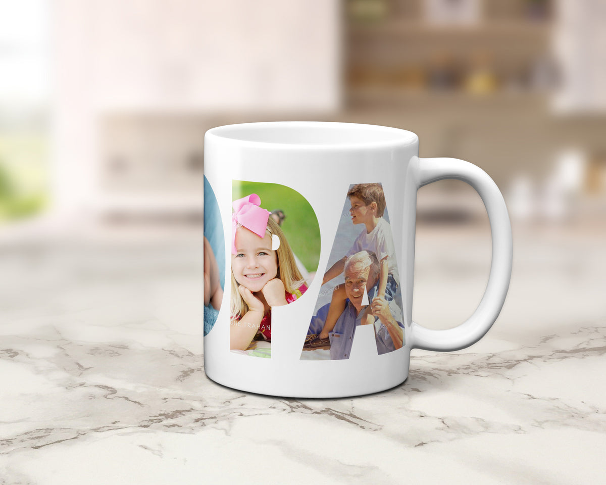 A white ceramic coffee mug with a custom photo collage print spelling 'GRANDPA', displayed on a light marble countertop with a blurred kitchen background.