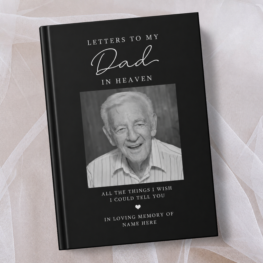 A black personalised keepsake book titled 'Letters to My Dad in Heaven' with a black and white portrait photo of an elderly man on the cover, photographed on soft white fabric.