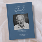 A personalised hardcover book titled 'Letters to My Dad in Heaven' with a slate blue cover, a black and white portrait photo of an elderly man, and white text, displayed on a soft beige fabric background.