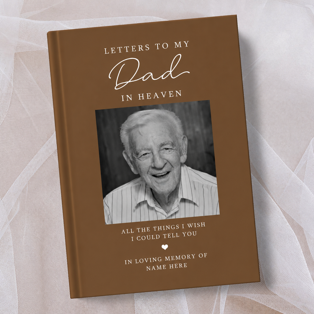A personalised hardcover book titled 'Letters to My Dad in Heaven' with a brown cover, a black and white portrait photo of an elderly man, and white text, displayed on a soft beige fabric background.