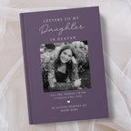 A personalised hardcover book with a muted purple cover, featuring a black and white photo of a young woman and placeholder text for a memorial letter to her in heaven, styled on a soft beige fabric background.