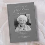 A personalised hardcover book titled 'Letters to My Grandma in Heaven' with a grey cover, a black and white photo of an elderly woman, and placeholder text for a memory tribute, styled on soft white tulle fabric.