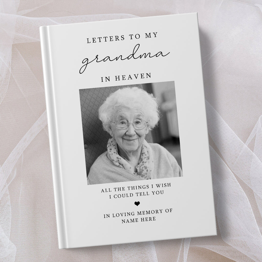 A personalised hardcover book titled 'Letters to My Grandma in Heaven' with a black and white portrait photo of an elderly woman on the cover, styled on a soft white fabric background.