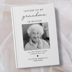 A personalised hardcover book titled 'Letters to My Grandma in Heaven' with a black and white portrait photo of an elderly woman on the cover, styled on a soft white fabric background.