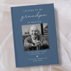 A personalised hardcover book titled 'Letters to My Grandpa in Heaven' with a slate blue cover, a black and white portrait photo of an elderly man, and white text, styled on a soft beige fabric background.