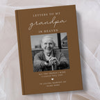 A personalised hardcover book titled 'Letters to My Grandpa in Heaven' with a brown cover, a black and white portrait photo of an elderly man, and white text, displayed on a soft white fabric background.