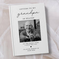 A personalised hardcover book titled 'Letters to My Grandpa in Heaven' with a black and white portrait photo of an elderly man on the cover, styled on a soft white fabric background.
