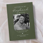 A personalised hardcover book titled 'Letters to My Husband in Heaven' in olive green, featuring a black and white photo of a smiling man and placeholder text, displayed on a soft beige fabric background.