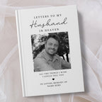 A personalised hardcover book titled 'Letters to My Husband in Heaven' with a black and white portrait photo of a smiling man on the cover, photographed on soft white tulle fabric.