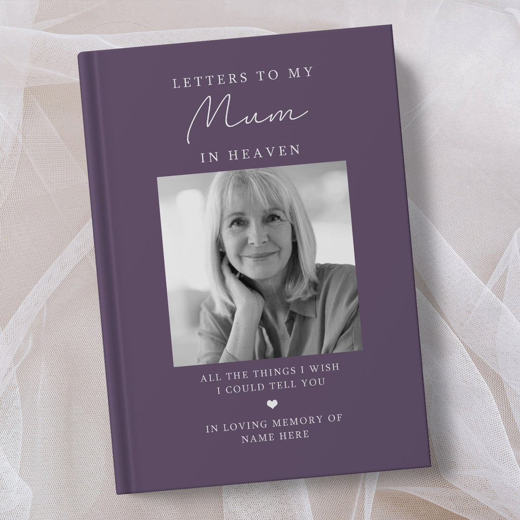 A personalised hardcover book titled 'Letters to My Mum in Heaven' in a muted purple colour, featuring a black and white portrait photo of a woman on the cover, displayed on a soft beige fabric background.