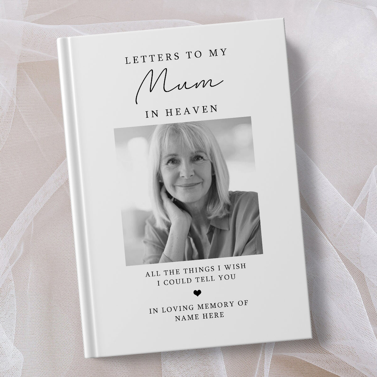 A personalised hardcover book titled 'Letters to My Mum in Heaven' with a black and white portrait photo of a woman on the cover, styled on a soft white fabric background.