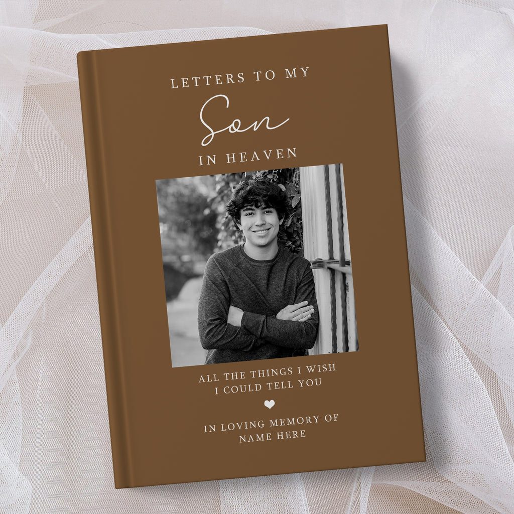 A personalised brown hardcover book titled 'Letters to My Son in Heaven' with a black and white photo of a young man on the cover, displayed on a soft white tulle fabric background.