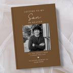 A personalised brown hardcover book titled 'Letters to My Son in Heaven' with a black and white photo of a young man on the cover, displayed on a soft white tulle fabric background.