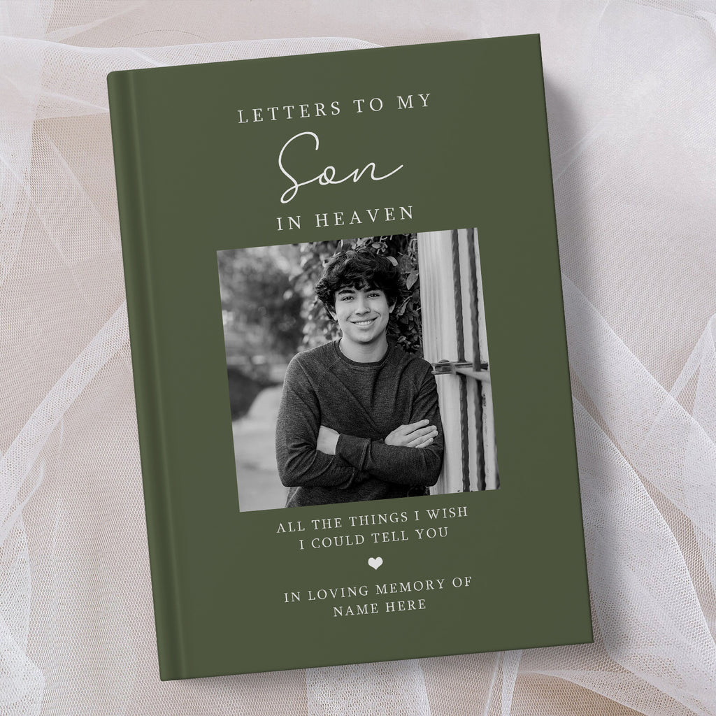 A personalised hardcover book titled 'Letters to My Son in Heaven' in olive green, featuring a black and white photo of a young man on the cover, displayed on a soft beige fabric background.