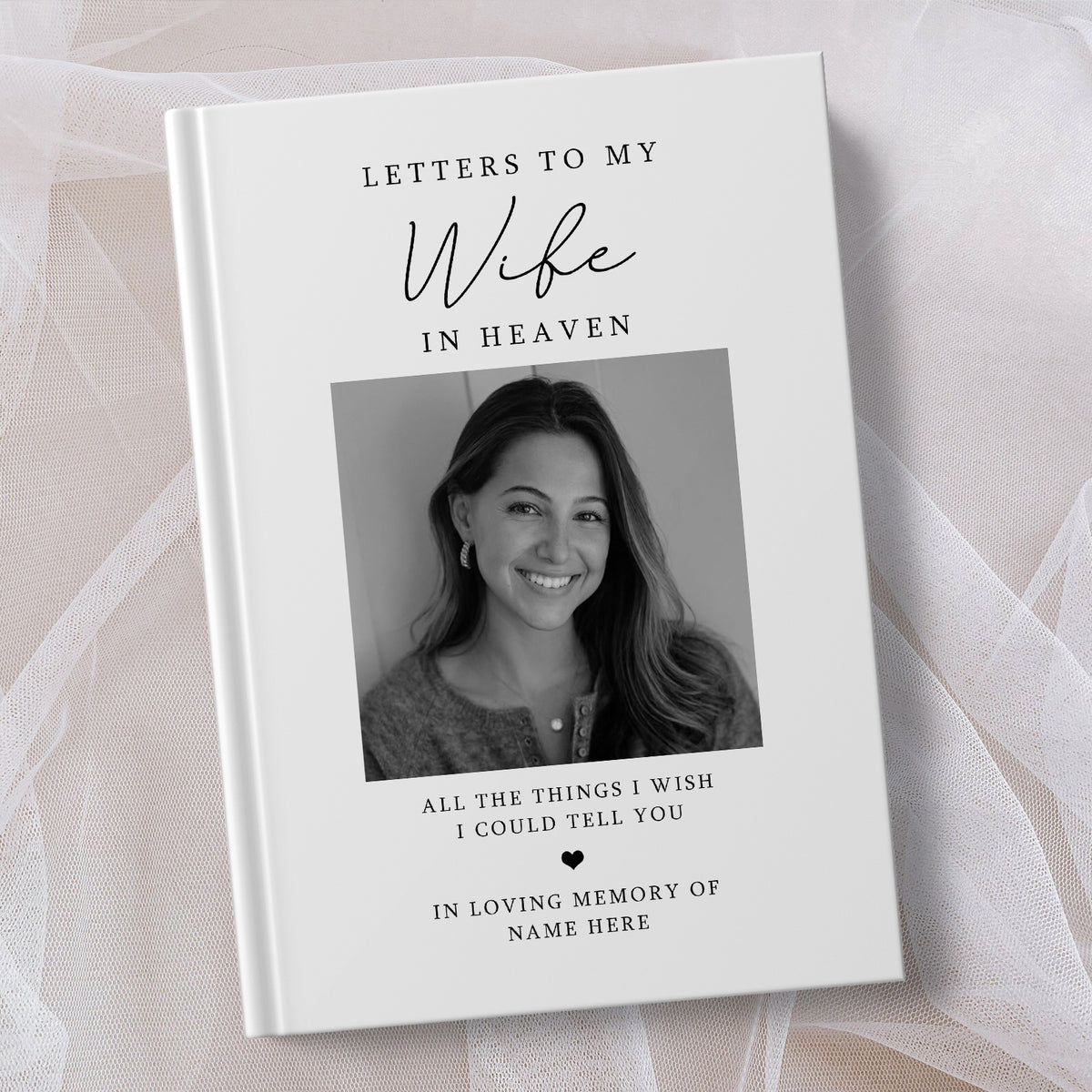 A personalised hardcover book titled 'Letters to My Wife in Heaven' with a black and white portrait photo on the cover, displayed on a soft white fabric background.
