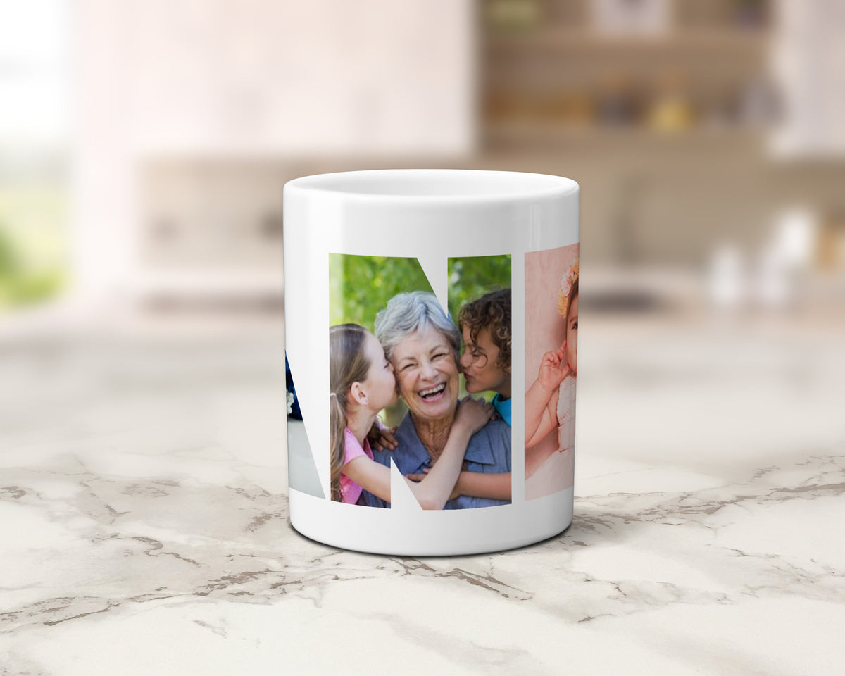 A white ceramic mug featuring a custom multi photo collage within the letters spelling NANNA, set on a light marble countertop with a blurred kitchen background.