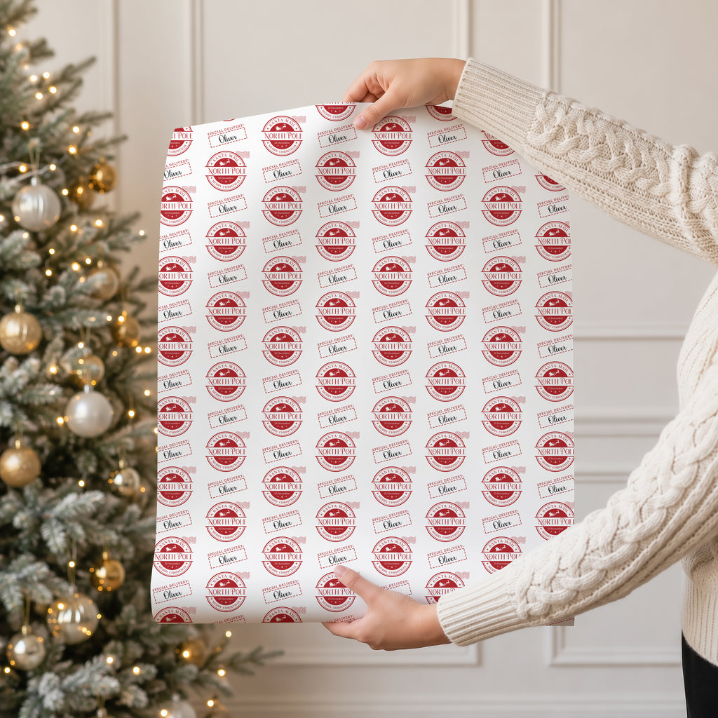 A person in a cream cable knit sweater holds up a sheet of wrapping paper featuring a repeating red and white circular stamp pattern. The background shows a decorated Christmas tree and a white panelled wall.