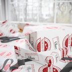 White wrapping paper with a red vintage Santa Claus stamp pattern, shown wrapped around gift boxes on a windowsill with scissors nearby.