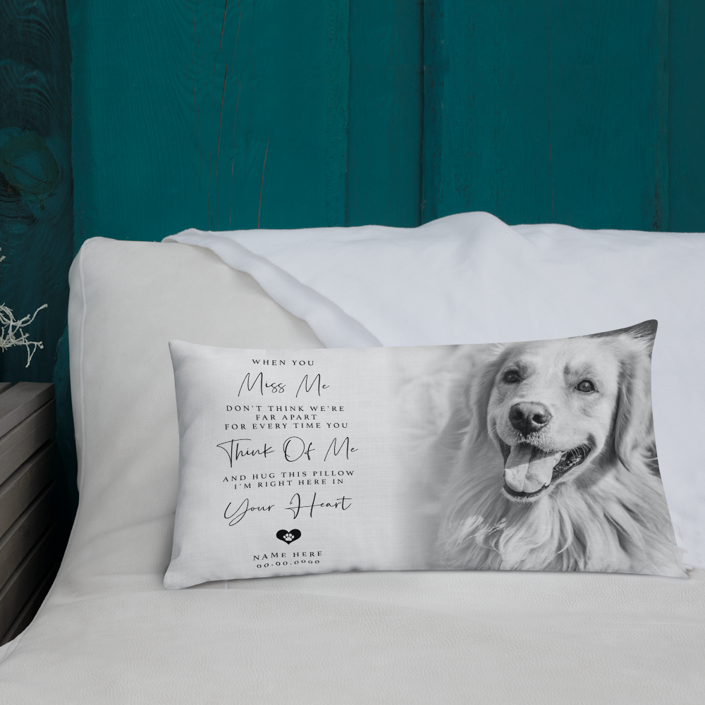 A rectangular personalised pet memorial pillow with a black and white photo of a dog and sentimental text, resting on white pillows against a dark teal wooden headboard.