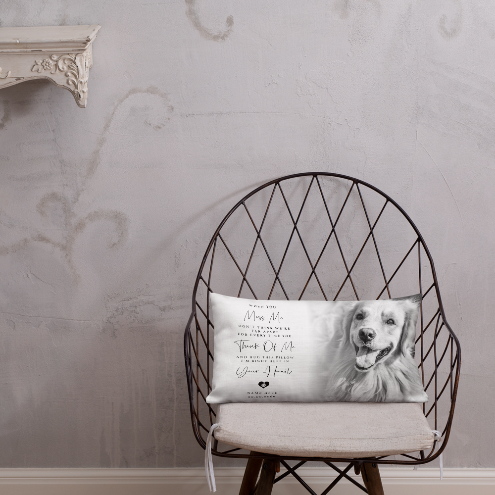 A rectangular personalised pet memorial throw pillow with a black and white photo of a golden retriever and printed text, resting on a black wire chair against a textured light grey wall.