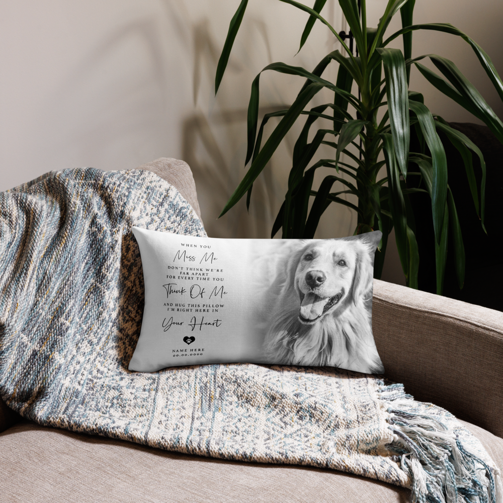 A rectangular pet memorial pillow featuring a black and white photo of a golden retriever and sentimental text, resting on a beige sofa draped with a blue and cream patterned throw blanket, next to a green houseplant.