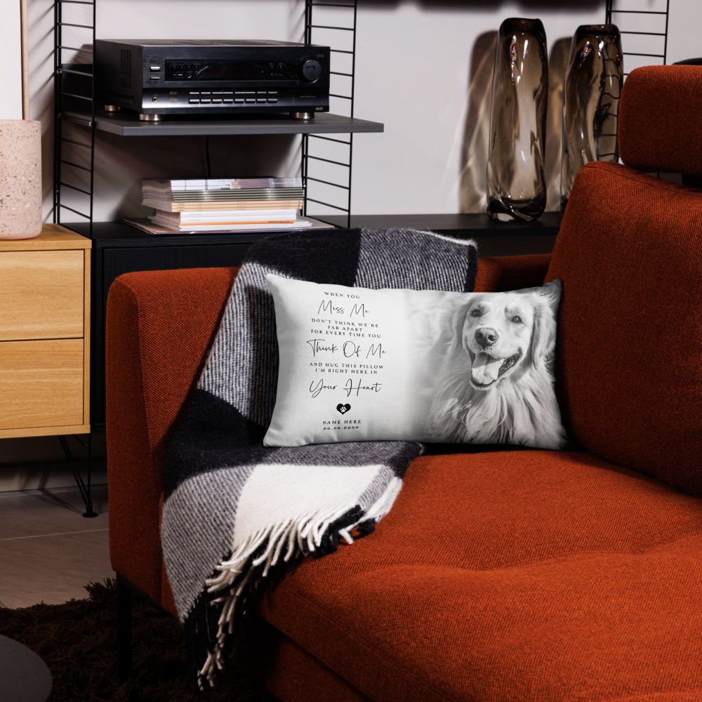 A rectangular personalised throw pillow with a black-and-white portrait of a golden retriever and printed memorial text, resting on a orange sofa draped with a black-and-white plaid blanket in a styled living room.