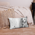 A rectangular personalised pet memorial pillow with a grayscale photo of a golden retriever and sentimental text, styled on a pink rug in front of a bed with a striped blanket.