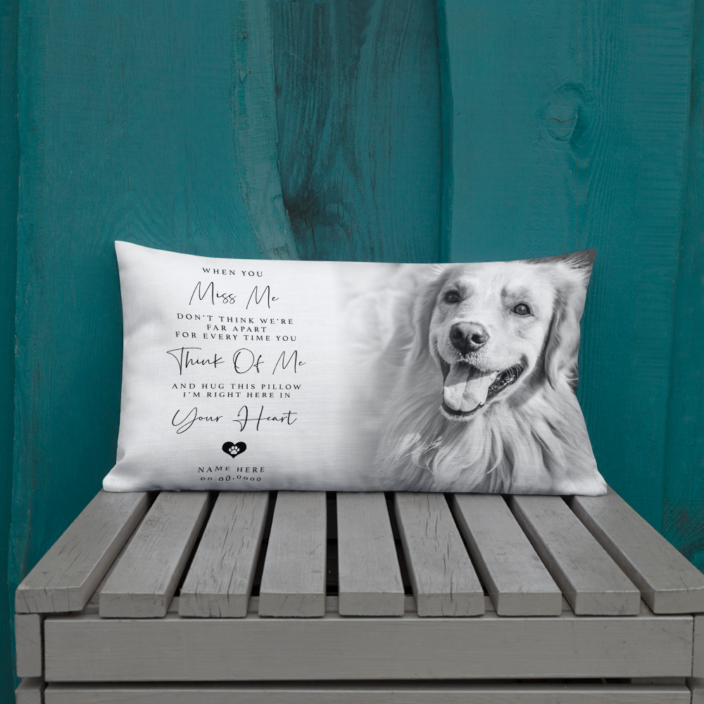 A rectangular personalised pet memorial throw pillow with a black and white photo of a golden retriever and sentimental text, displayed on a grey wooden bench against a teal wooden wall.
