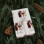 A gift box wrapped in twine, displayed on a bed of green pine needles with pinecones. The wrapping paper features festive illustrations of Santa Claus and reindeer with the text 'MERRY CHRISTMAS Matilda'.