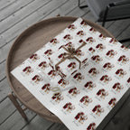A gift wrapped box and a roll of matching wrapping paper displayed on a round wooden tray. The wrapping paper has a repeating print of a red and gold Santa Claus and Reindeer illustration with the name 'Matilda' written below each figure, and the box is tied with a brown ribbon.