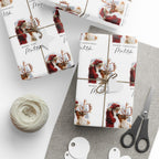 Three wrapped gift boxes with matching Christmas themed wrapping paper are arranged on a light grey surface with twine, a ball of string, scissors, and white tags. The wrapping paper has a white background with a repeating print of Santa Claus in a red coat and reindeer, plus 'MERRY CHRISTMAS' text.