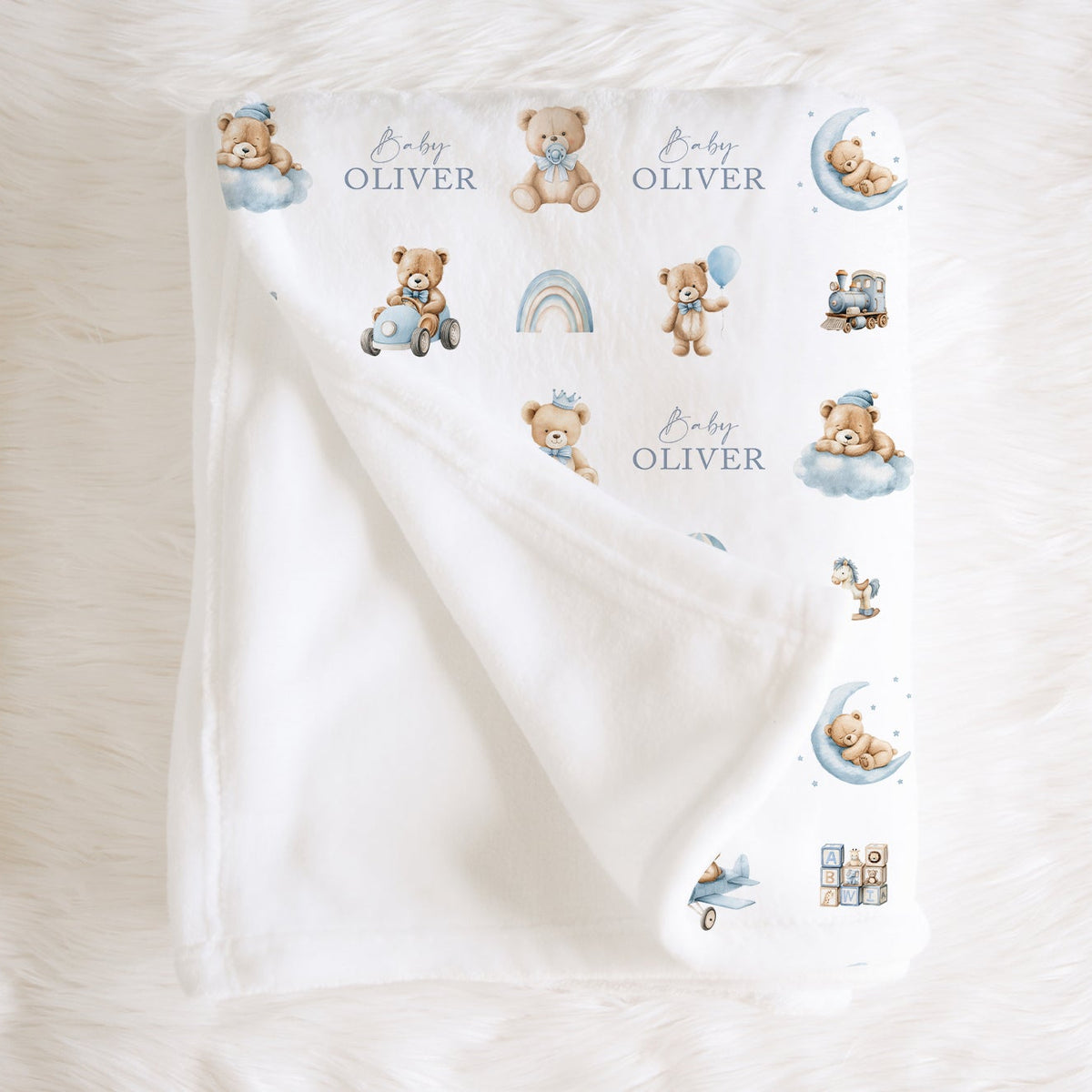 A personalised white baby blanket with teddy bear illustrations, personalised with the name 'Oliver', folded on a white faux fur background.