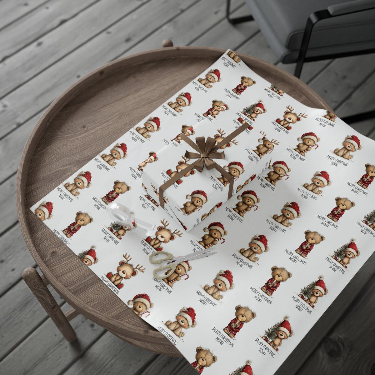 White wrapping paper with a repeating pattern of teddy bears in Santa hats and Christmas outfits, shown wrapped around a gift box on a round wooden tray over gray deck flooring.