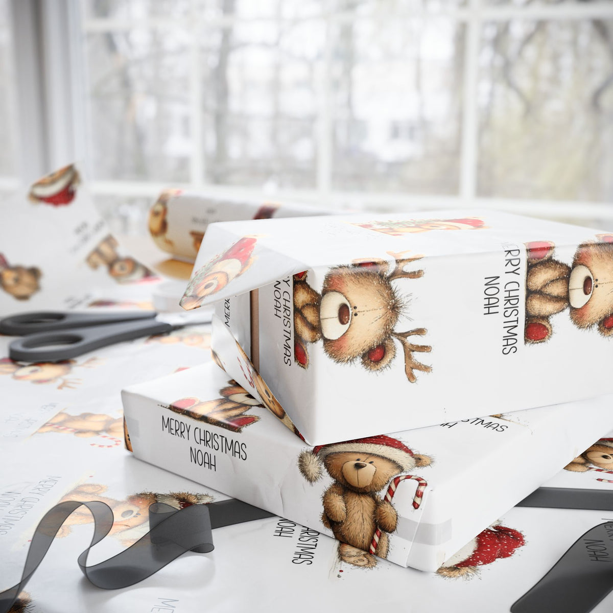 White Christmas themed wrapping paper with teddy bear illustrations and the text 'MERRY CHRISTMAS NOAH', shown wrapped around gift boxes on a table with scissors and ribbon nearby.