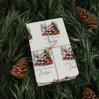 A gift box with personalised Christmas gift wrap with twine, featuring a festive holiday illustration of Santa Claus, reindeer, pine trees, and the name 'Evelyn' on a white background, styled on green pine branches with pinecones.